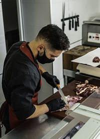 Professional butcher with mask cutting raw meat