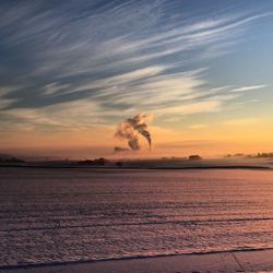 View of calm sea with smoke stack in distance