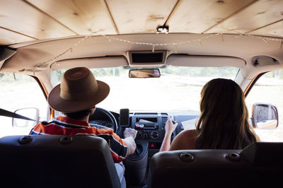 Back view of anonymous couple of travelers riding van and enjoying road trip in summer