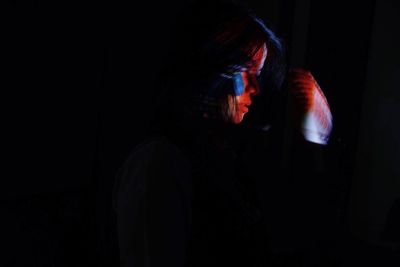 Portrait of young woman standing against black background