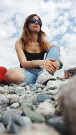 Low angle view of young woman wearing sunglasses while sitting against sky