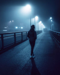 Rear view of man standing on illuminated road at night