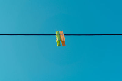 Low angle view of clothespins hanging on rope against blue sky