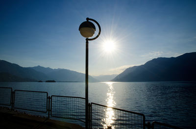 Street light by sea against sky during sunset