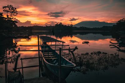 Boat moored in lake against sky during sunset