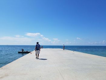 Rear view of man walking on pier at sea against sky