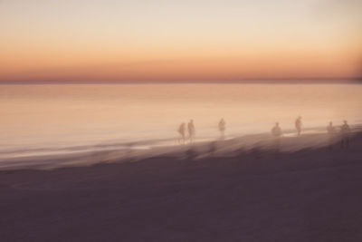 Silhouette people on beach against sky during sunset