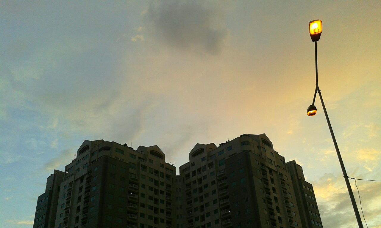 low angle view, street light, sky, architecture, building exterior, built structure, lighting equipment, cloud - sky, city, illuminated, dusk, cloudy, sunset, cloud, electricity, outdoors, cable, no people, building, high section