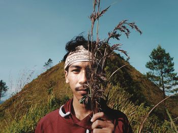 Portrait of young man holding plant against clear sky