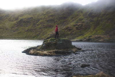 Rear view of woman standing on rock by sea against sky