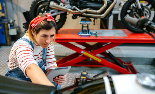 Mechanic with digital tablet reviewing information of motorcycle on garage