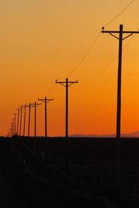 Silhouette electricity pylons against orange sky