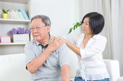 Woman giving shoulder massage to father while sitting on sofa at home