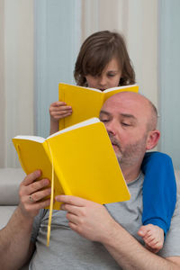 Father and son together enjoying reading and discussing school homework from yellow textbook.