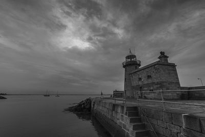 Building by sea against cloudy sky