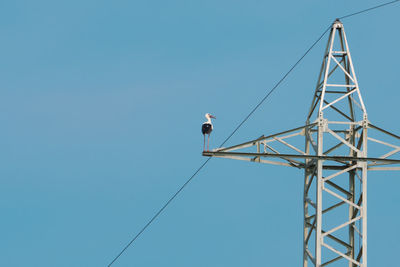 Low angle view of electricity pylon against clear blue sky