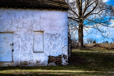 Old house by bare tree on field against sky