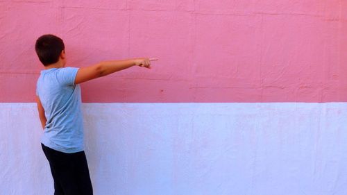 Rear view of boy pointing while standing by wall