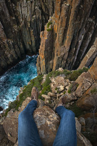 Low section of man sitting on cliff against valley