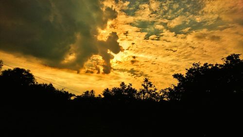Low angle view of dramatic sky over silhouette trees