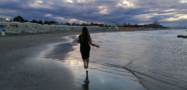 Rear view of woman walking on beach against sky