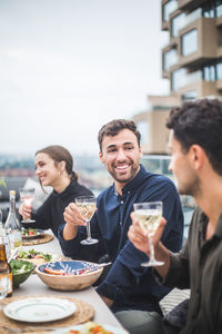 Smiling man talking to friend while sitting by woman during party on rooftop