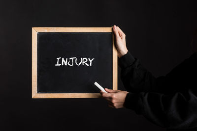 Midsection of man holding blackboard against black background