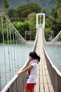 Young woman standing on rope bridge over river