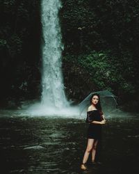 Full length of woman standing by waterfall in forest