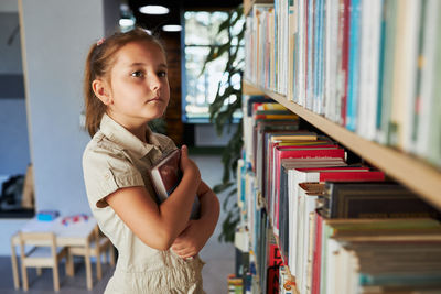 School girl looking at bookshelf in school library. smart girl selecting literature for reading