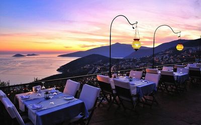 Dinning table at sidewalk cafe by mountains and sea during sunset