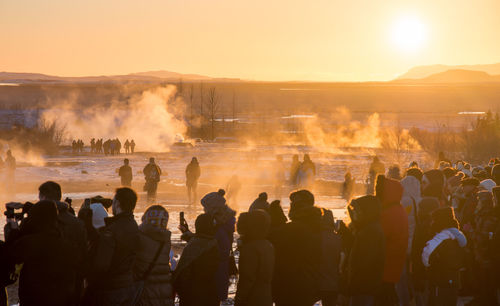 People by hot springs against sky during sunset