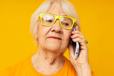 Smiling senior woman talking on phone against yellow background