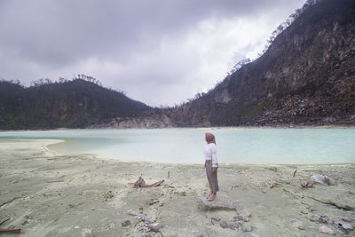 Beautiful asian girl standing on the stone at kawah putih or white volcanic crater lake in ciwidey