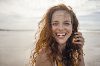 Portrait of a redheaded woman, laughing happily on the beach