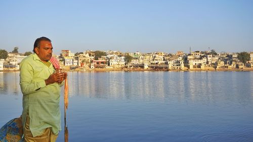 Man standing by river against sky in city