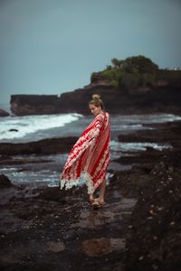 Woman standing on rock at beach against sky