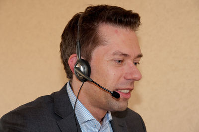 Close-up of businessman using headphones against wall