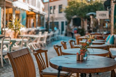 Empty chairs and tables at sidewalk cafe against buildings