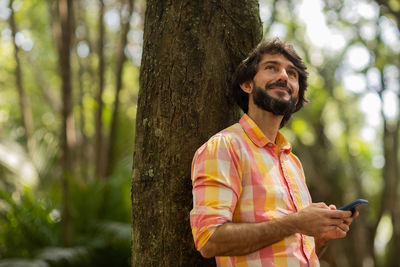 Young man with smartphone at day time with a green park in the background. mobile phone, technology,