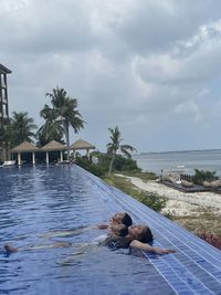 People relaxing in swimming pool by sea against sky