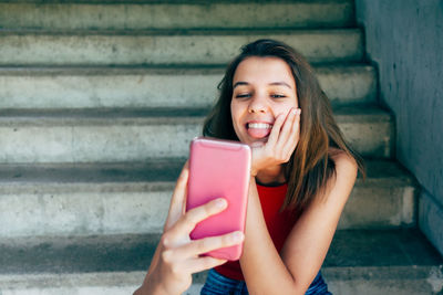 Portrait of happy woman holding smart phone while sitting on staircase