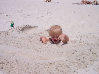 High angle view of girl crying while buried in sand at beach on sunny day
