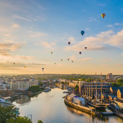 Hot air balloons flying over city against sky during sunset