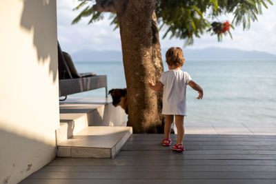 Infant child walk alone to the sea in tropical hotel. little girl rear view