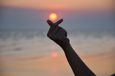 Low angle view of hand holding sun against sky during sunset