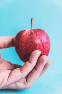 Close-up of hand holding apple against blue background