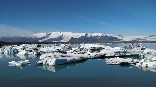 Scenic view of frozen lake by snow covered mountain against sky