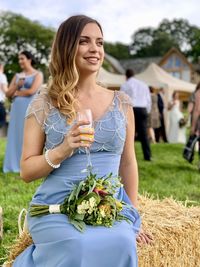 Bride holding champagne flute while sitting on hay and looking away