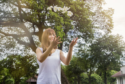 Low angle view of young woman throwing white flowers in yard